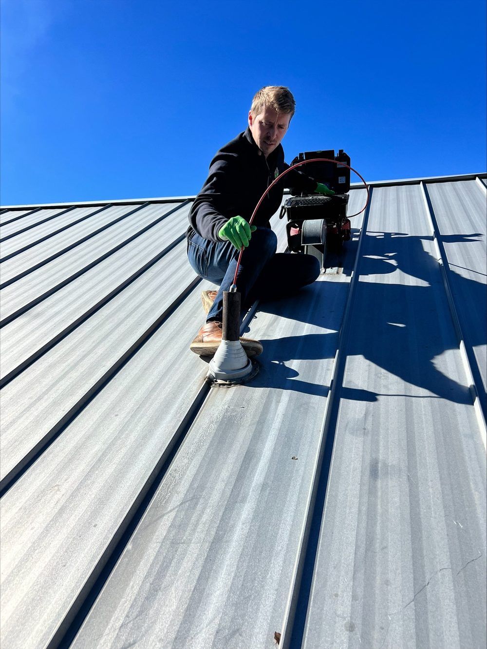 HouseScan inspector crouching on a metal roof with a sewer scope camera