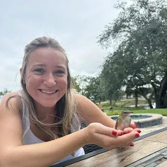 HouseScan team member smiling while gently holding a small bird beside a backyard pool