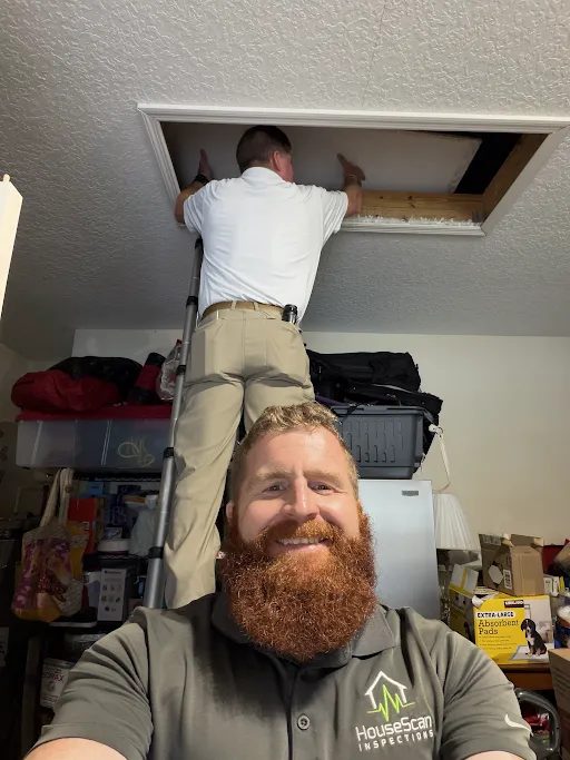 HouseScan inspector taking a selfie while a colleague on a ladder checks an attic opening