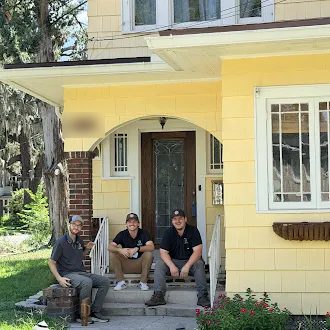 Three HouseScan inspectors sitting on the front steps of a yellow house